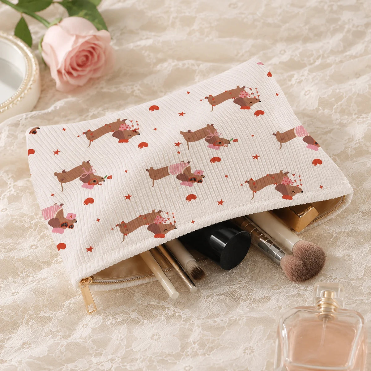 A beige corduroy cosmetic bag with a floral pattern and a gold zipper, lying on lace fabric next to makeup brushes.