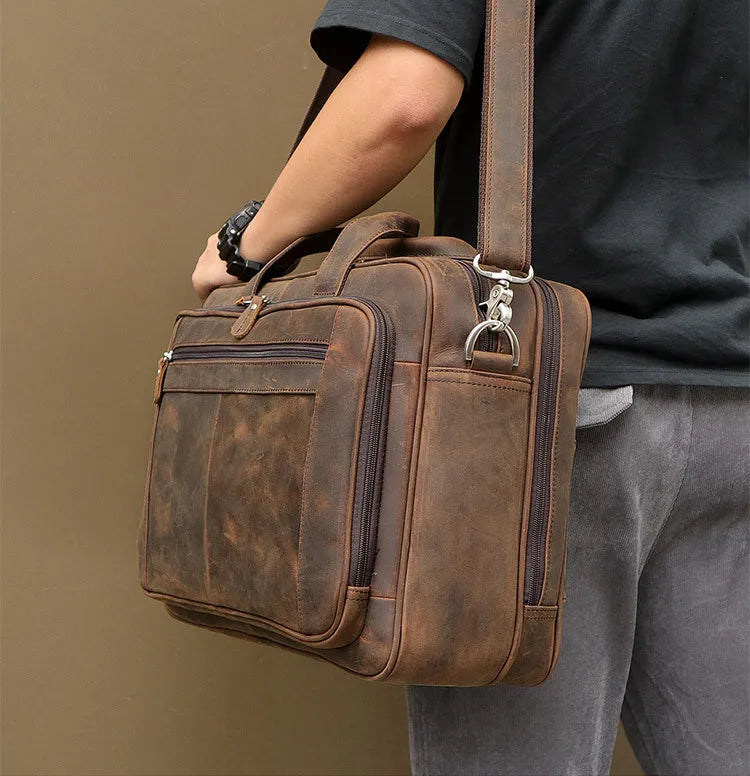 A brown genuine leather briefcase with dark stitching is carried by a person wearing a black shirt and gray pants.