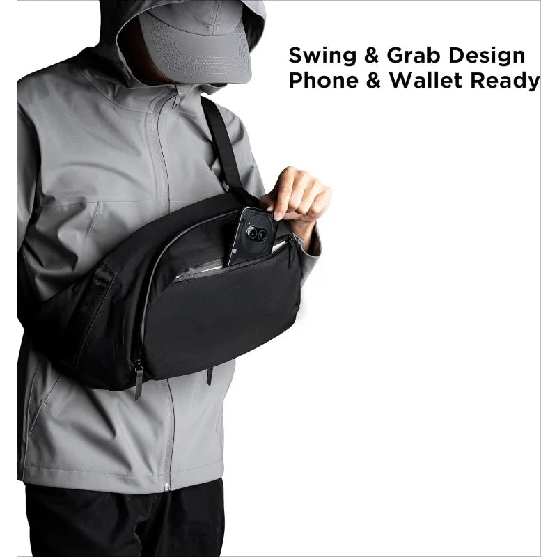 A person wearing a gray jacket is demonstrating a black sling bag designed for phone and wallet access.
