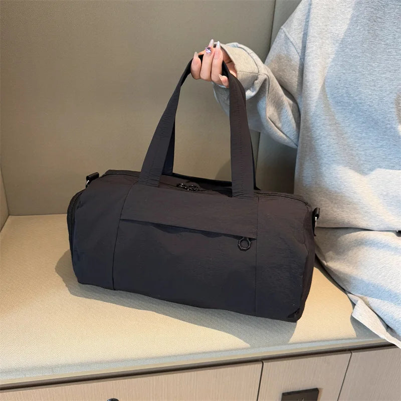 A dark gray Oxford gym duffel bag is shown resting on a light-colored surface next to a person's arm.
