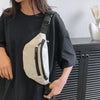 A person is holding a beige nylon waist bag with black zippers against a black t-shirt.