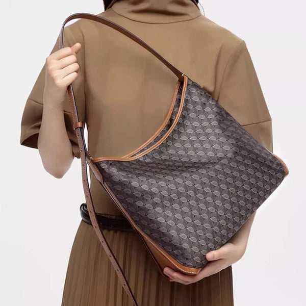A woman holds a brown geometric embroidery hobo shoulder bag with a leather strap against a neutral colored top.