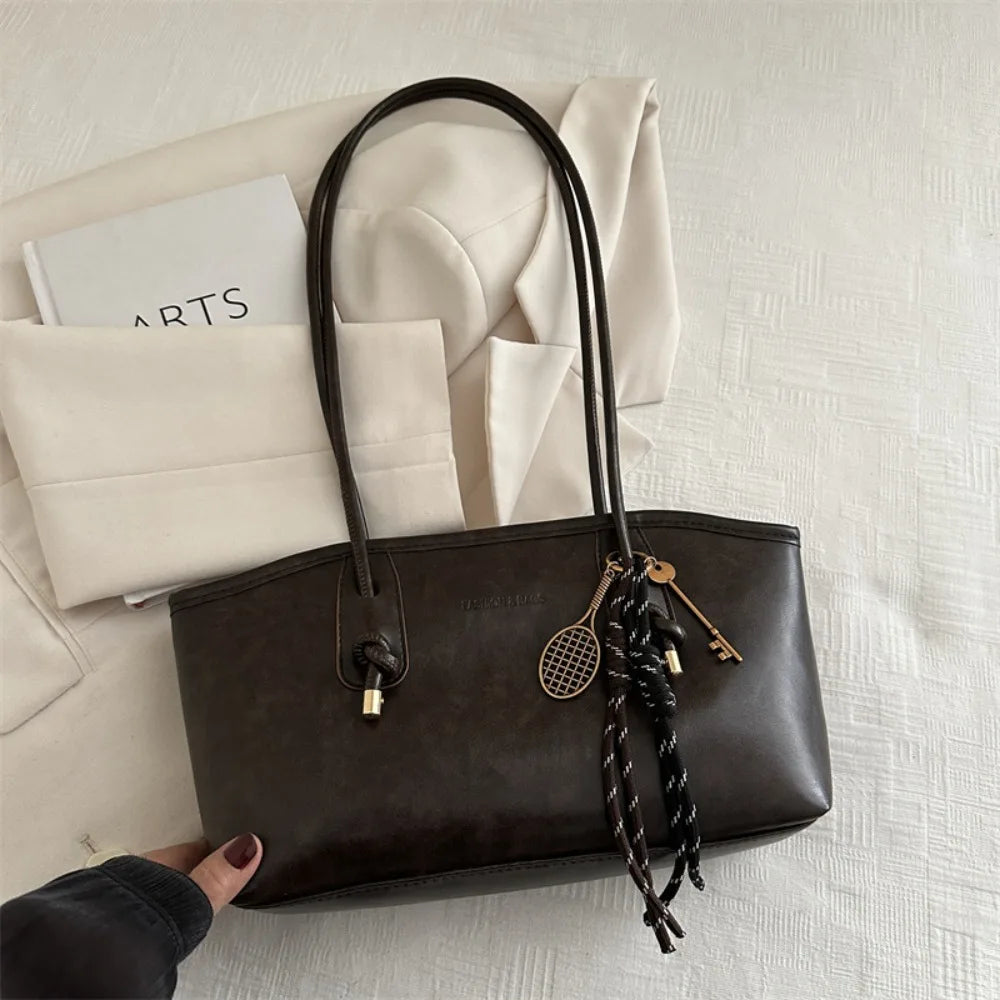 A dark brown PU leather tote bag with black leather handles and gold hardware resting on a white textured surface.