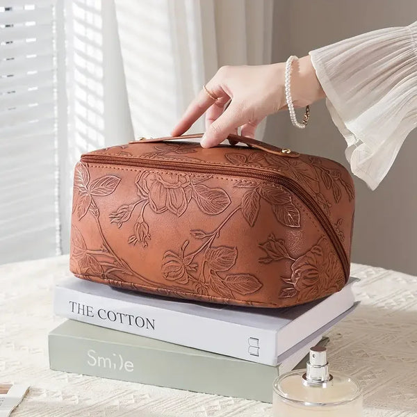 A hand holds a vintage floral waterproof makeup tote bag with rose gold hardware resting on a stack of books.