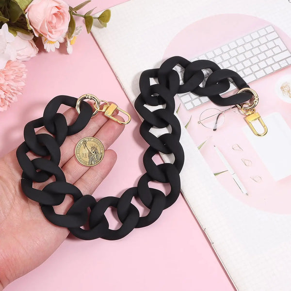 Correa de cadena de acrílico negro con cierres dorados mostrada sobre un fondo rosa.