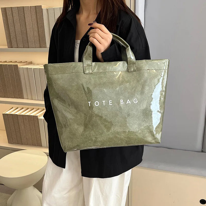 A person holds a transparent waterproof PVC tote bag with a green tint against a light background.