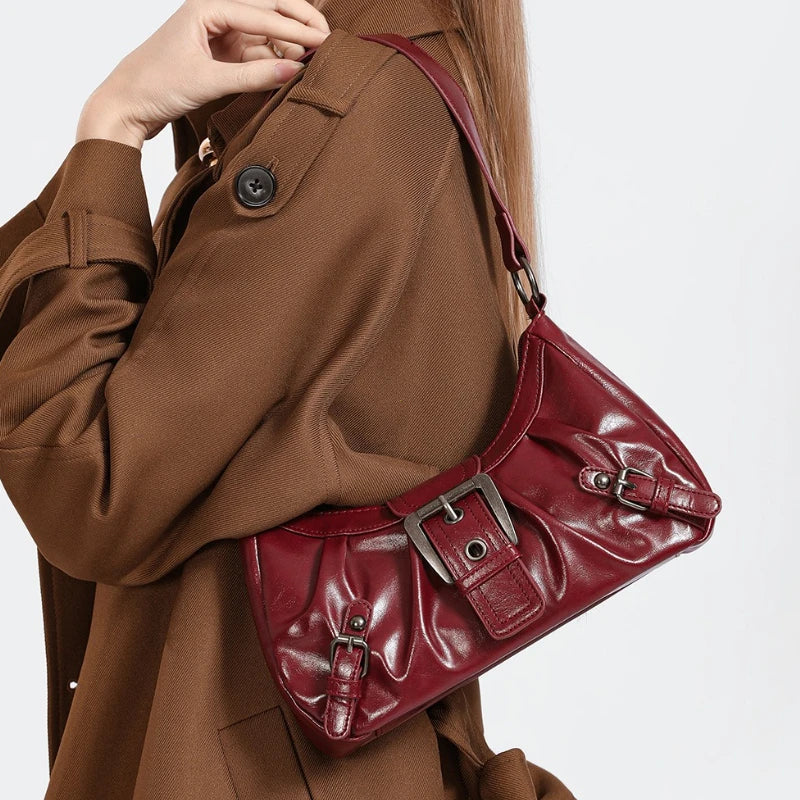 Nahaufnahme einer dunkelroten, plissierten Leder-Schultertasche, getragen von einer Person in einem braunen Mantel.