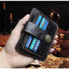 A hand holds a black genuine leather card wallet with multiple credit cards and an embossed leather strap.