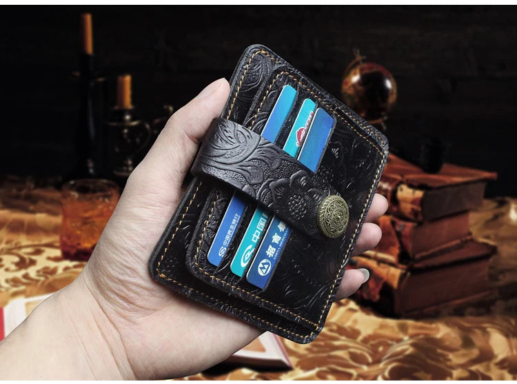 A hand holds a black genuine leather card wallet with multiple credit cards and an embossed leather strap.