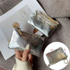 A silver metallic leather compact coin purse and key holder is shown being held against a gray fabric background.