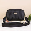 Schwarze gesteppte minimalistische Crossbody-Tasche mit goldener Akzent, auf einer weißen Fläche neben einem aufgerollten Buc