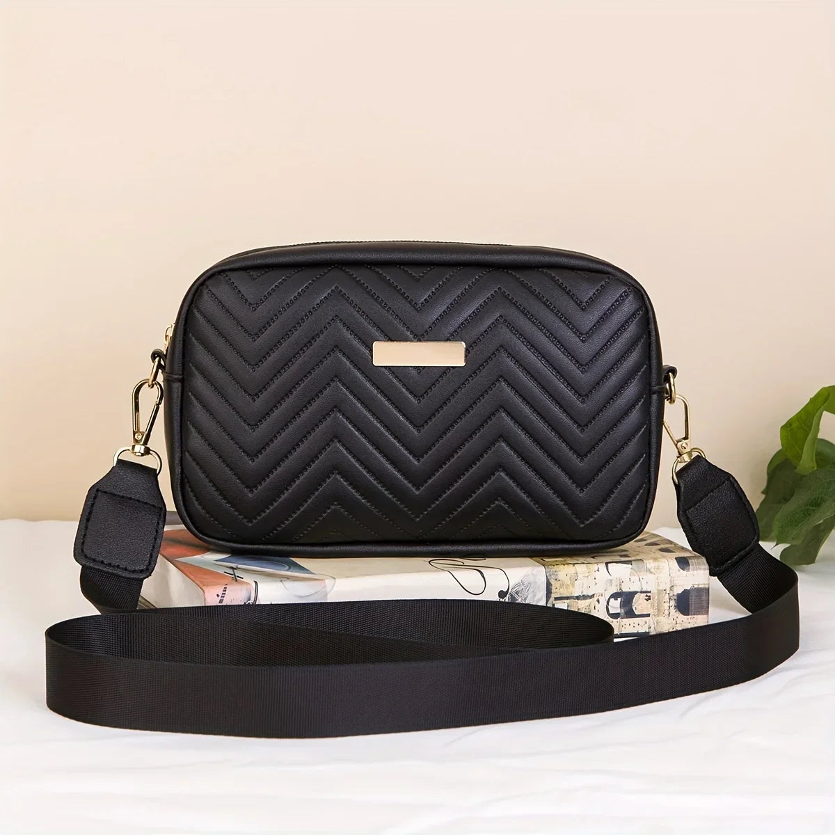 Schwarze gesteppte minimalistische Crossbody-Tasche mit goldener Akzent, auf einer weißen Fläche neben einem aufgerollten Buc
