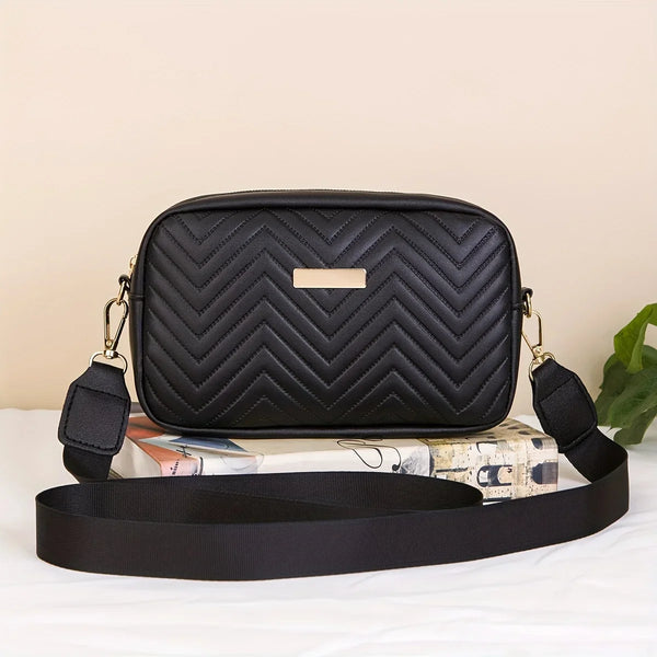 Schwarze gesteppte minimalistische Crossbody-Tasche mit goldener Akzent, auf einer weißen Fläche neben einem aufgerollten Buc