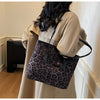 A woman holds a black leopard print vintage tote bag against a light beige coat.