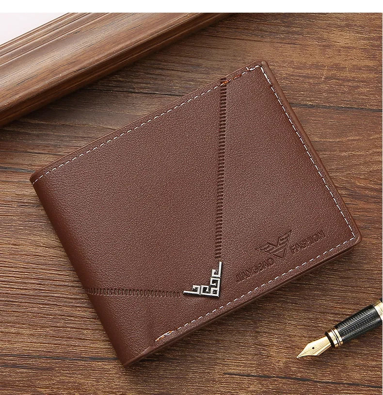 A brown men's slim leather bi-fold wallet resting on a wooden surface next to a pen.
