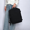 Ein schwarzer Reise-Rucksack wird von einer Person in weißem Hemd und blauen Jeans gehalten.