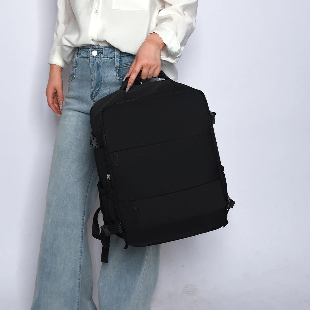 Ein schwarzer Reise-Rucksack wird von einer Person in weißem Hemd und blauen Jeans gehalten.