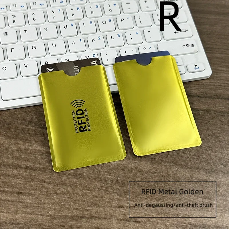 Two gold RFID metal card sleeves placed on a wooden surface next to a white laptop keyboard.