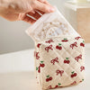 A hand holds a quilted storage pouch with a cherry and bow print, showing the fabric texture and design.