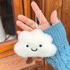A white cloud-shaped plush keychain with black eyes and a silver chain is held in a person's hand.