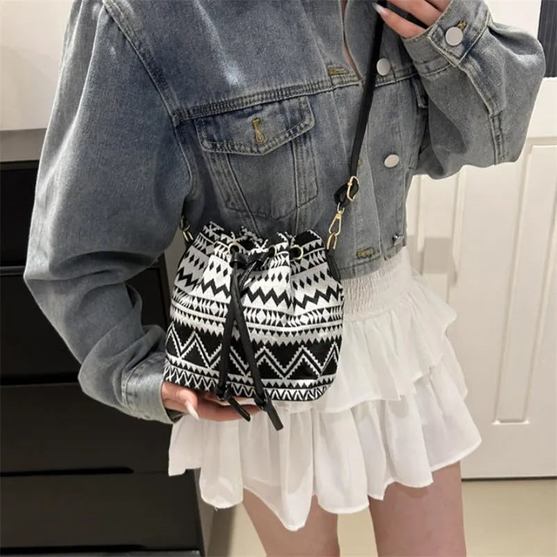 A person holds a black and white patterned drawstring bucket bag against a denim jacket and a white skirt.