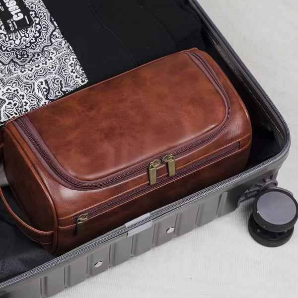 A brown leather toiletry bag with brass hardware is shown open inside a gray case.