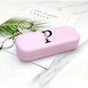 A pink hard shell eyeglass case with a letter charm rests on a white marble surface next to a pair of eyeglasses.