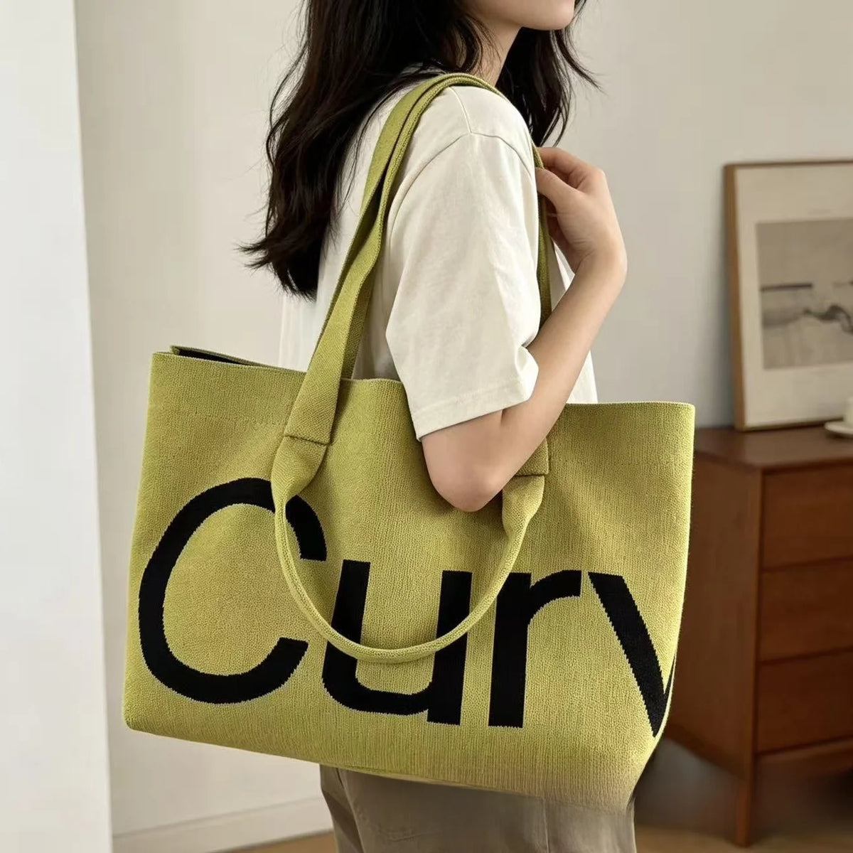 A woman holds a lime green knitted large tote bag with a black strap.