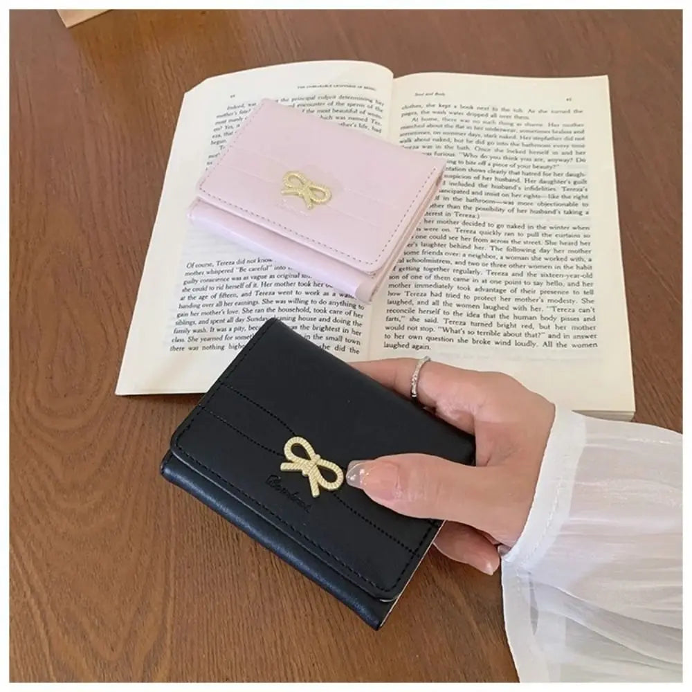 Cartera de cuero PU negra plegable con hebilla decorativa dorada sobre una mesa de madera junto a un libro abierto.