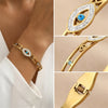 A close-up of a gold cuff bracelet featuring an evil eye crystal design with blue accents.