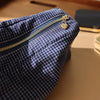 Pochette de rangement cosmétique en tissu à carreaux bleu foncé avec fermeture éclair dorée et charm sur une surface en bois.