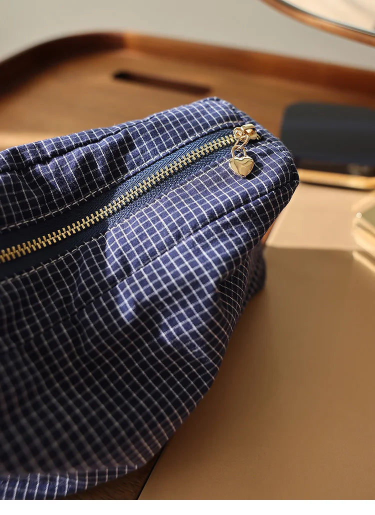 Pochette de rangement cosmétique en tissu à carreaux bleu foncé avec fermeture éclair dorée et charm sur une surface en bois.