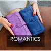 A purple and blue clutch wallet is held by a person on a wooden table.