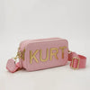 A pink leather pouch bag with gold lettering featuring the name KURT and a matching strap.