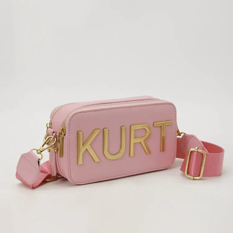 A pink leather pouch bag with gold lettering featuring the name KURT and a matching strap.