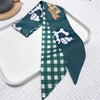 Une cravate de soie vert foncé avec un motif panda blanc et une étiquette dorée, présentée sur une assiette blanche.