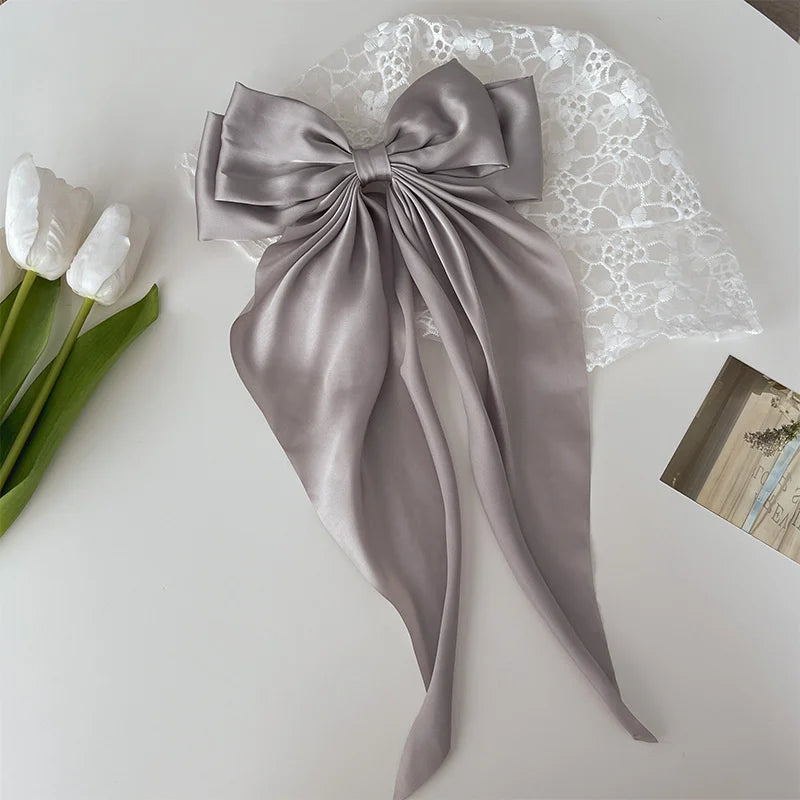 A silver silk bow tied in a large bow shape rests on white lace fabric next to white tulips.