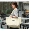 A woman models a beige Lee oxford cloth tote bag in an outdoor setting.