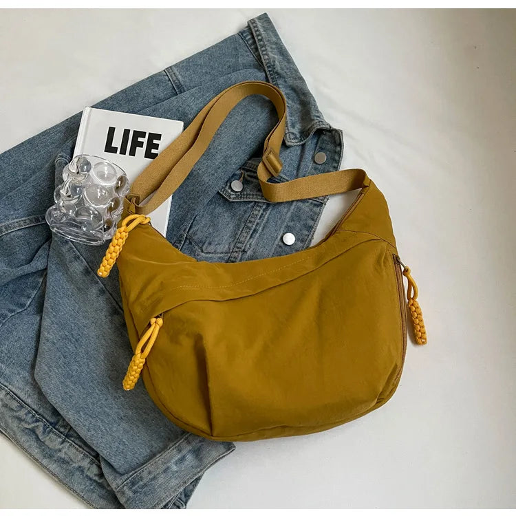 Senffarbener Nylon-Crossbody-Bag auf einem Stapel Jeans.
