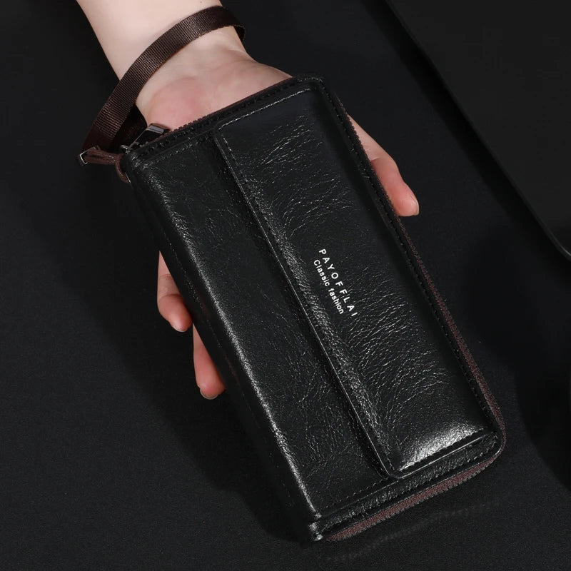 Une main tient un porte-monnaie à clochette en cuir noir avec une sangle marron et du texte gravé.