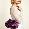 A woman models a white dress and a purple rose floral evening clutch bag with a chain strap.