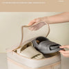 A hand is opening a beige portable luggage shoe organizer bag to show the upper shoe slot and half-mesh pocket.