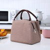 A brown and white striped thermal lunch bag with a handle is placed on a white countertop next to kitchen appliances.