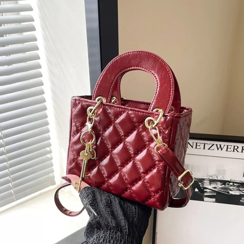 A maroon quilted leather crossbody handbag with gold chain accents is displayed next to a window.