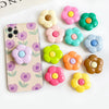 A collection of colorful, flower-shaped silicone phone grips and ring stands arranged on a white surface.