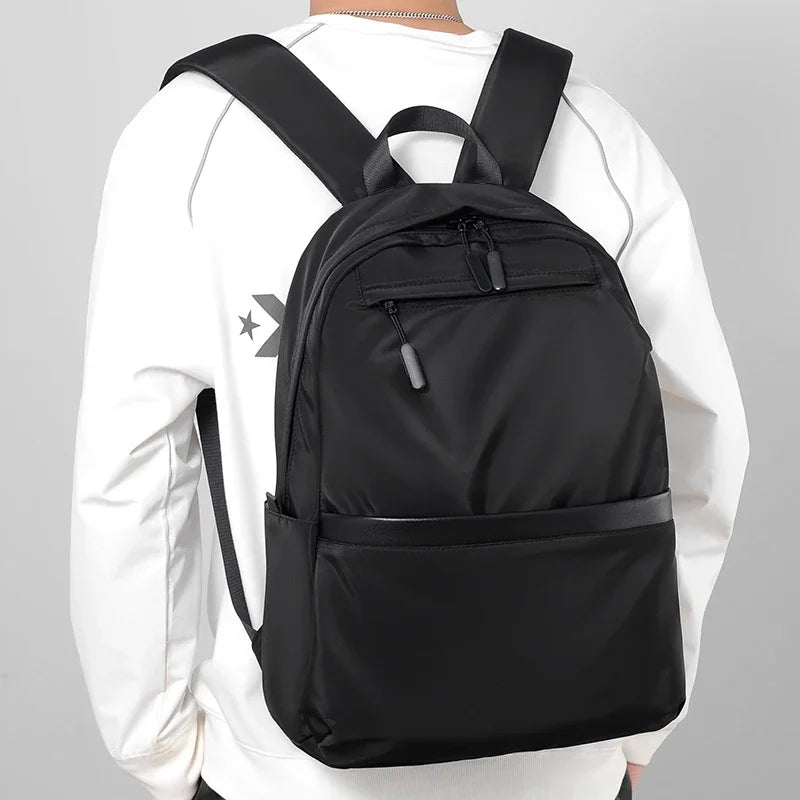 A black men's lightweight laptop backpack worn by a person in a white long-sleeved shirt.