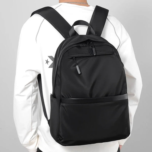 A black men's lightweight laptop backpack worn by a person in a white long-sleeved shirt.