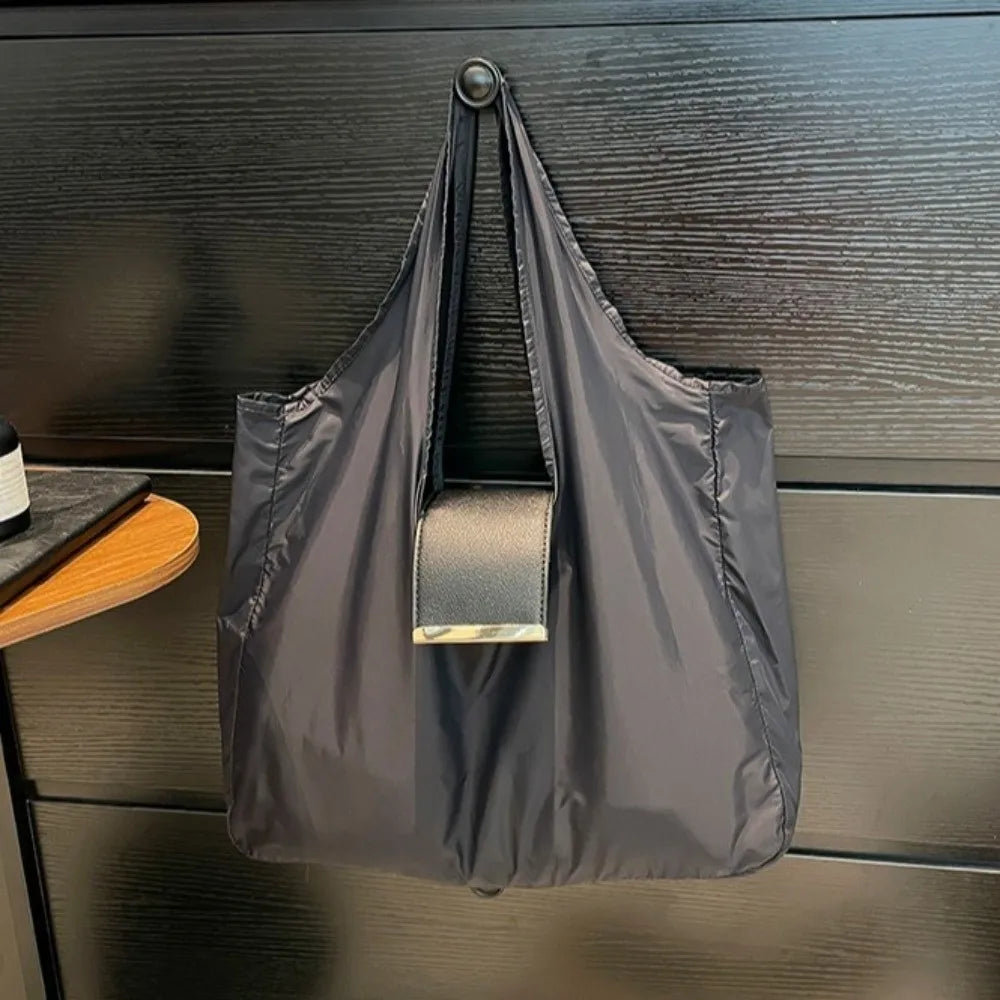 A dark gray foldable mini keychain tote bag hanging on a wooden surface.