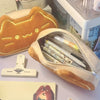 A tan caramel cat plush pencil pouch with a zipper is shown next to a white plastic clip.