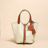 Beige Leder-Bucketbag mit braunen Ledergriffen und Zierleisten, vor hellem Hintergrund.